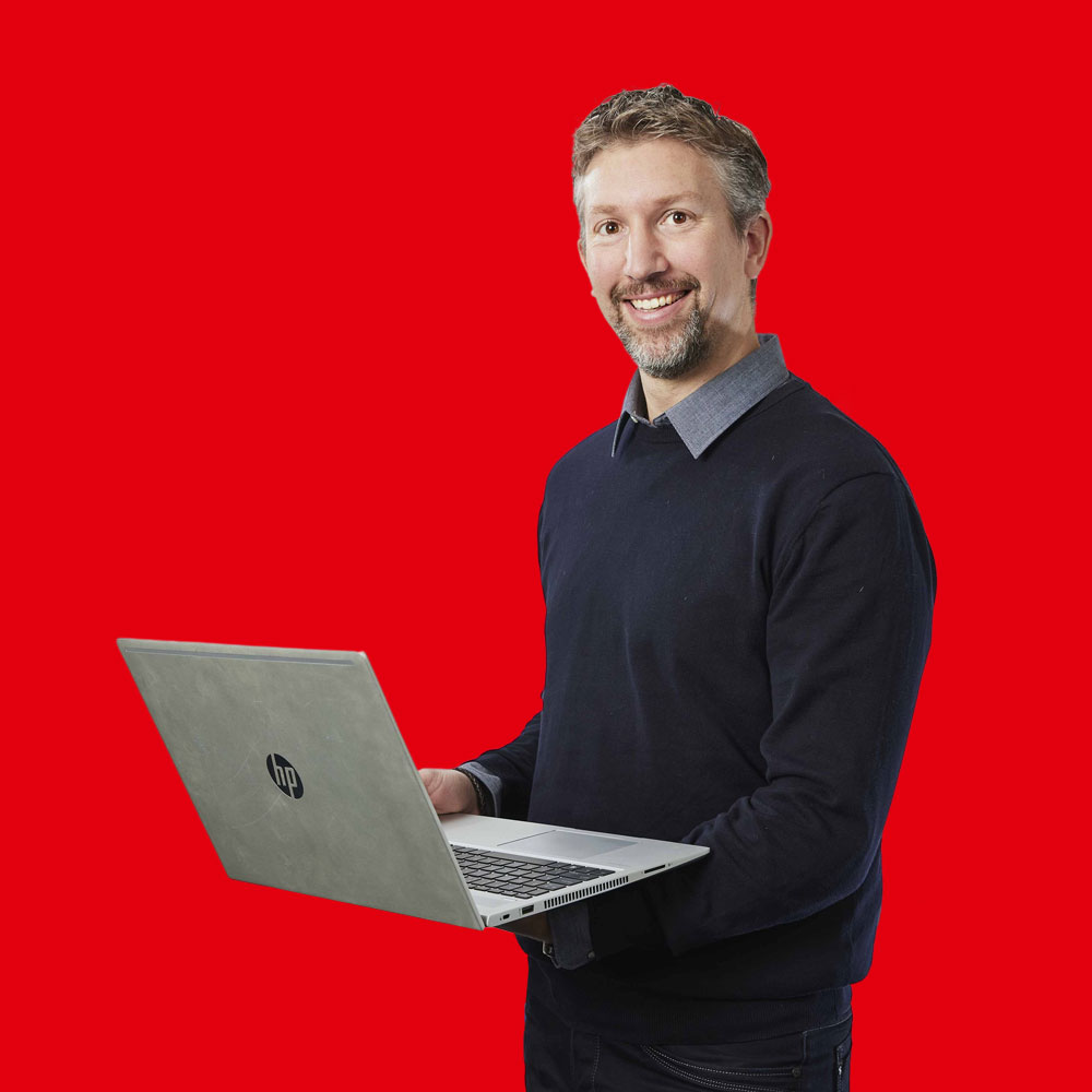Eddie-de-Boer heer met een donkerblauw vest en grijze blouse met een telefoon in zijn hand