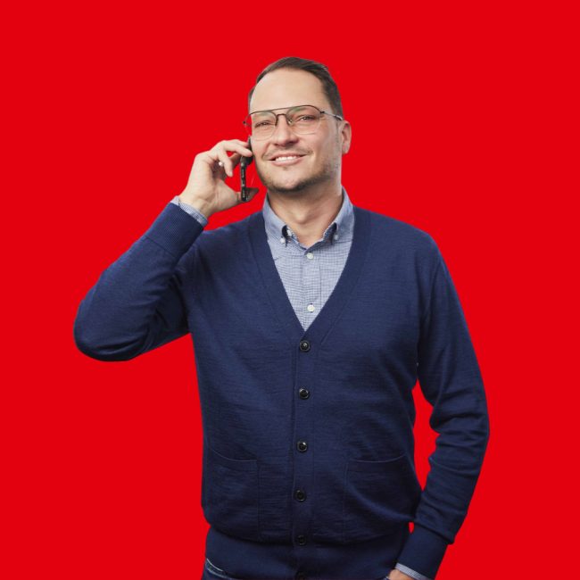 Franklyn-Wolf heer met een donkerblauw vest en lichtblauwe blouse met een telefoon in zijn hand