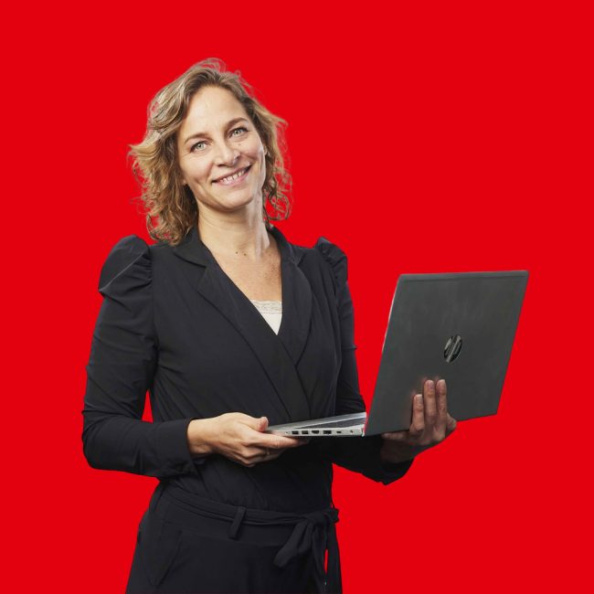 Marieke-Rink dame met blond in een zwarte jumpsuit die een laptop vasthoudt